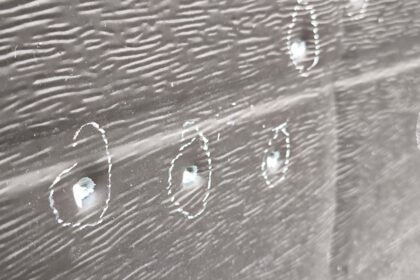 Close-up of a dark wooden plank with white chalk circles around small holes or screws