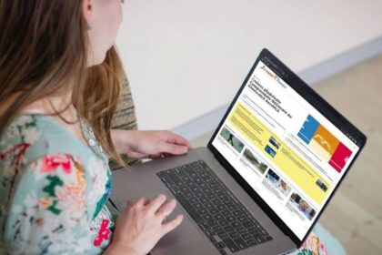 Woman in a floral dress typing on a silver laptop, looking at a colorful website on the screen.