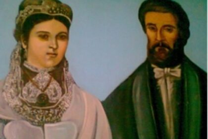 Portrait of a woman in an ornate headdress and white gown beside a bearded man in a dark suit against a blue background.