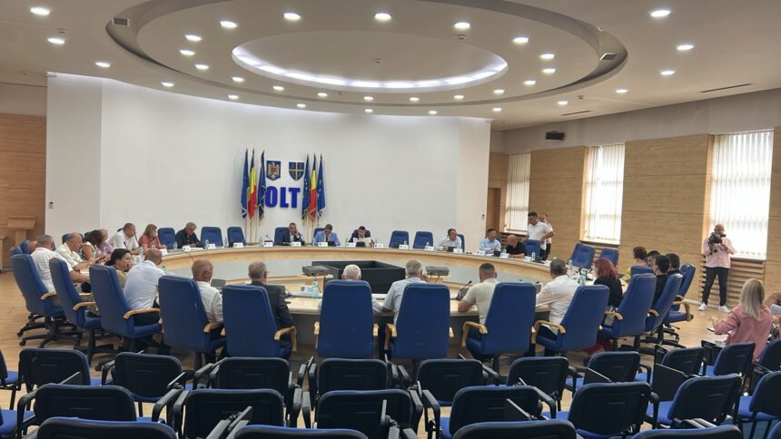 Officials sit around a large circular conference table in a bright meeting room; flags and a blue 'OLT' sign adorn the back wall, with a photographer on the right.