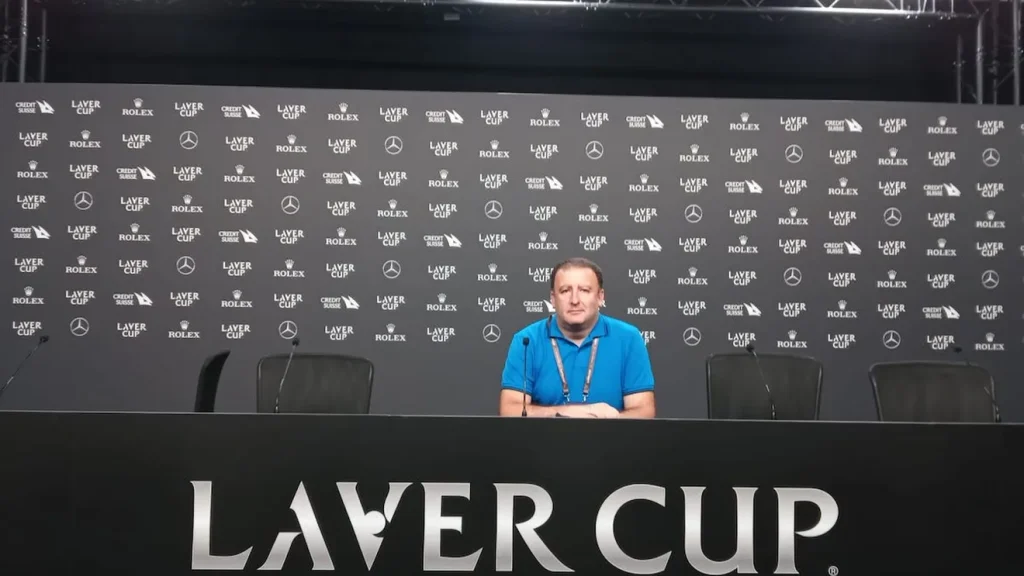Man in a blue polo sits at a press conference table with a Laver Cup backdrop behind him.