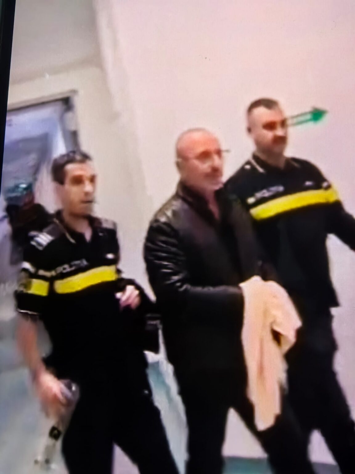 Three men in black jackets with yellow stripes stand indoors in a blurred group photo.