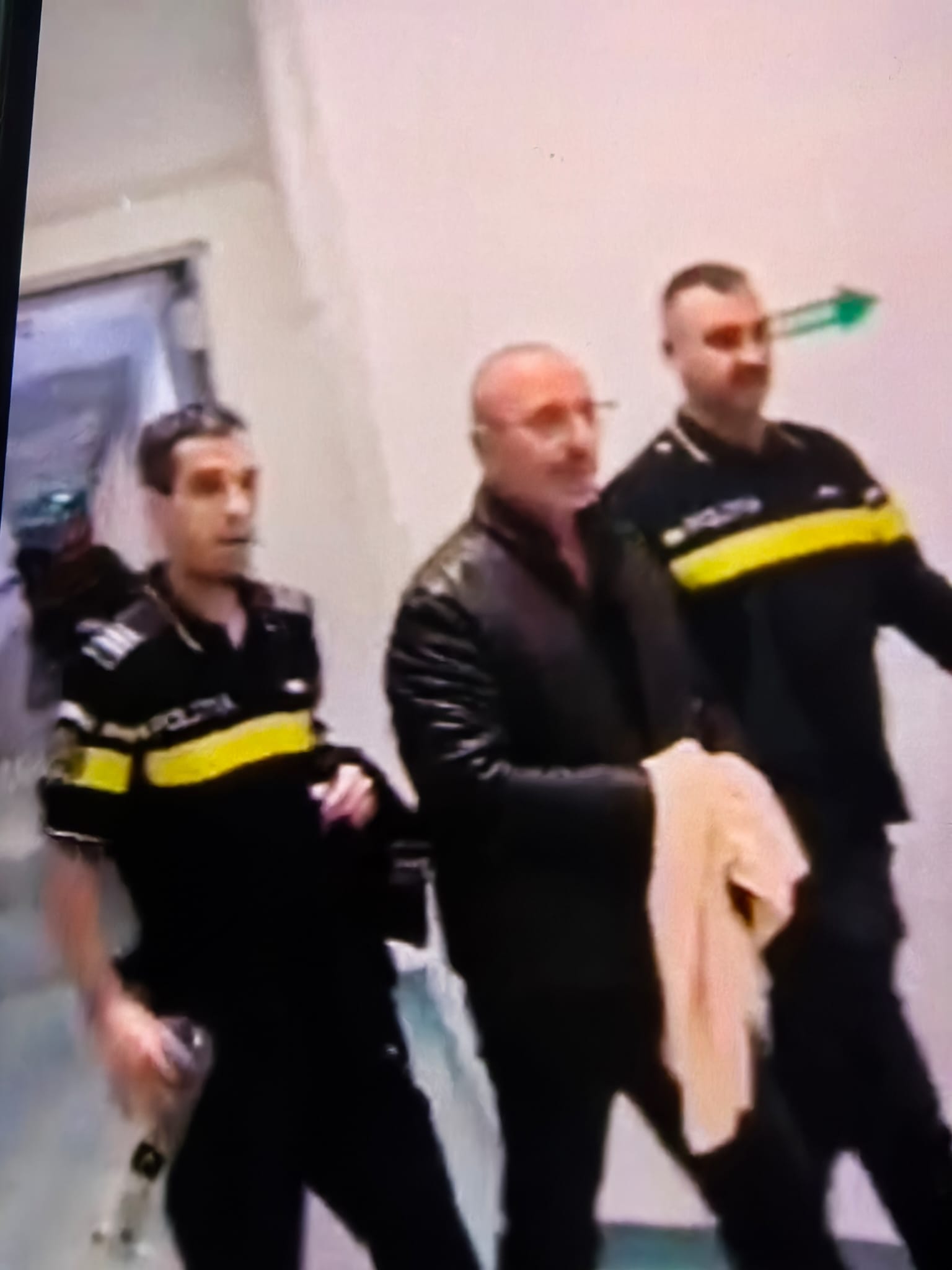 Three men in black jackets with yellow stripes stand indoors in a blurred group photo.