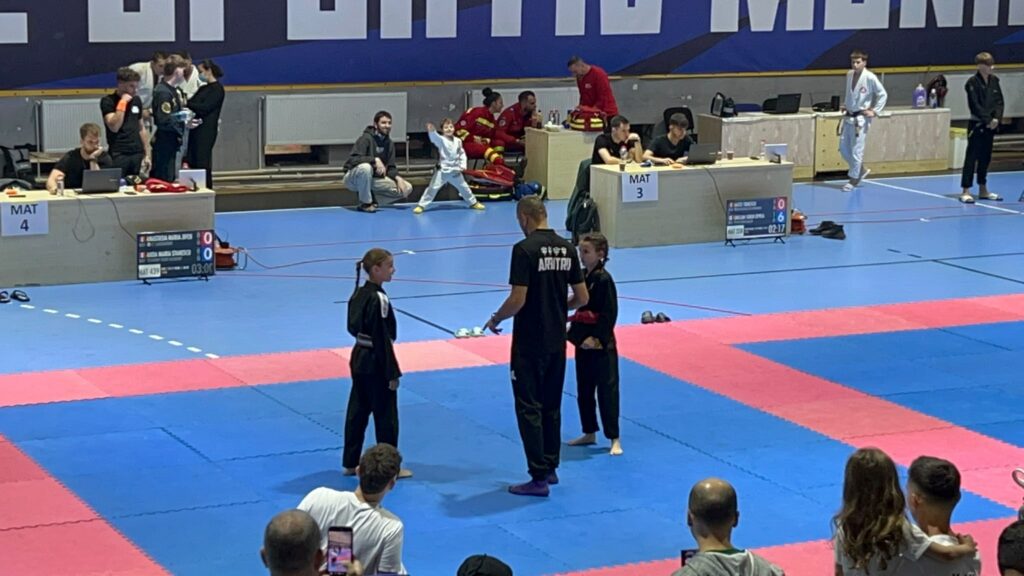 Martial arts tournament in a gym: young competitors in white gis near judges at MAT 3 and MAT 4 with a scoreboard and audience