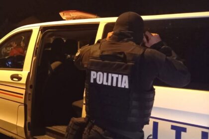 Officer in tactical gear standing by a police van at night, opening the side door to enter or check the vehicle.