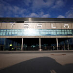 Tesla storefront with a wide glass facade and people waiting outside on a sunny day.