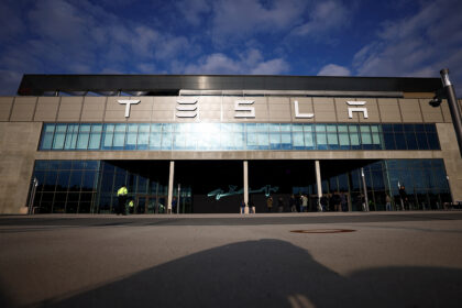 Tesla storefront with a wide glass facade and people waiting outside on a sunny day.