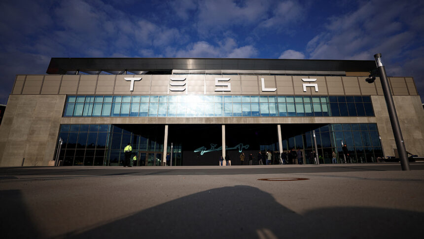 Tesla storefront with a wide glass facade and people waiting outside on a sunny day.