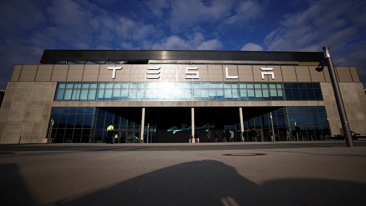 Tesla storefront with a wide glass facade and people waiting outside on a sunny day.