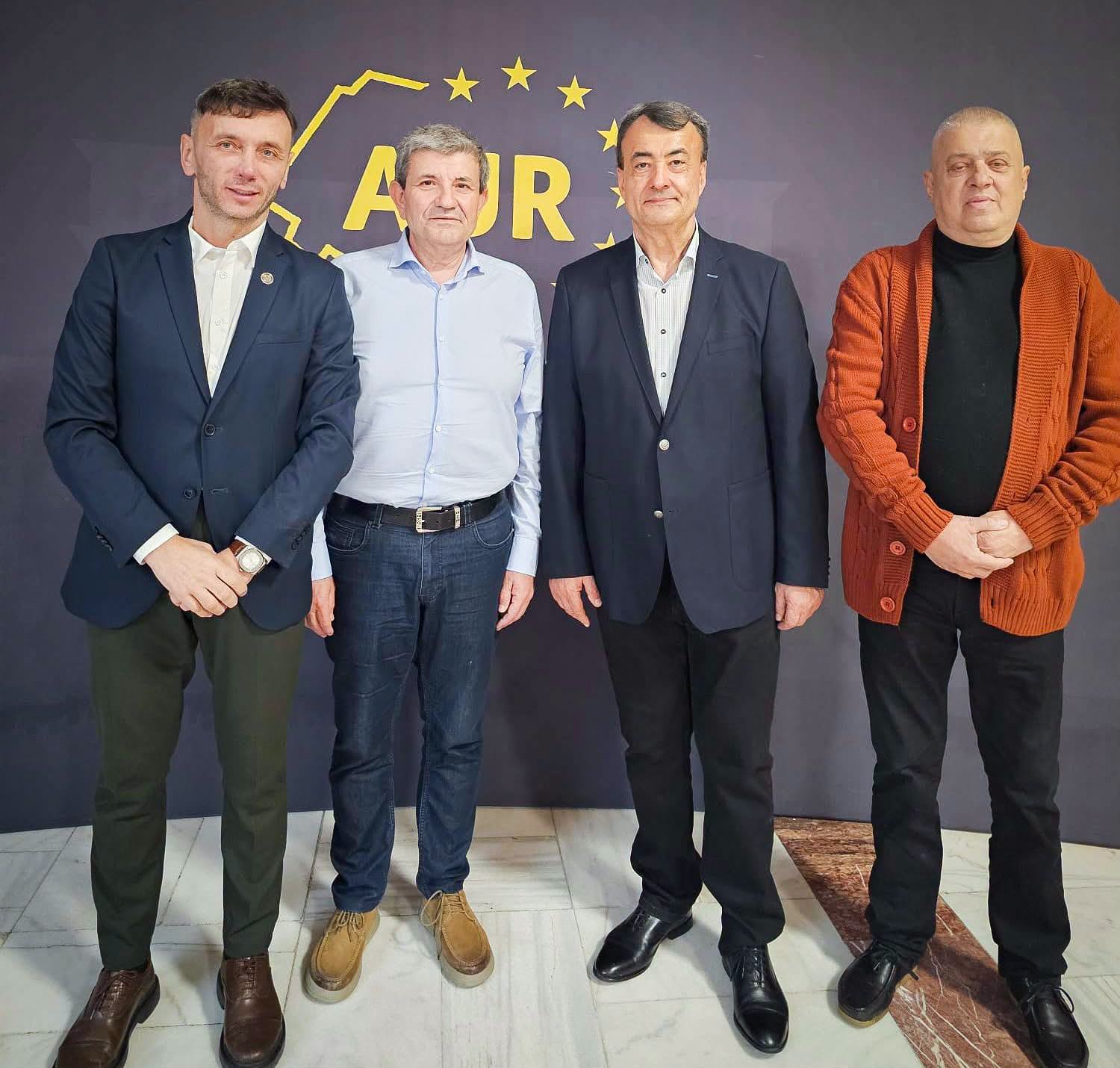 Group portrait of four men standing side by side indoors, dressed in blazers and smart casual wear, in front of a dark backdrop with a yellow ADR logo and stars.