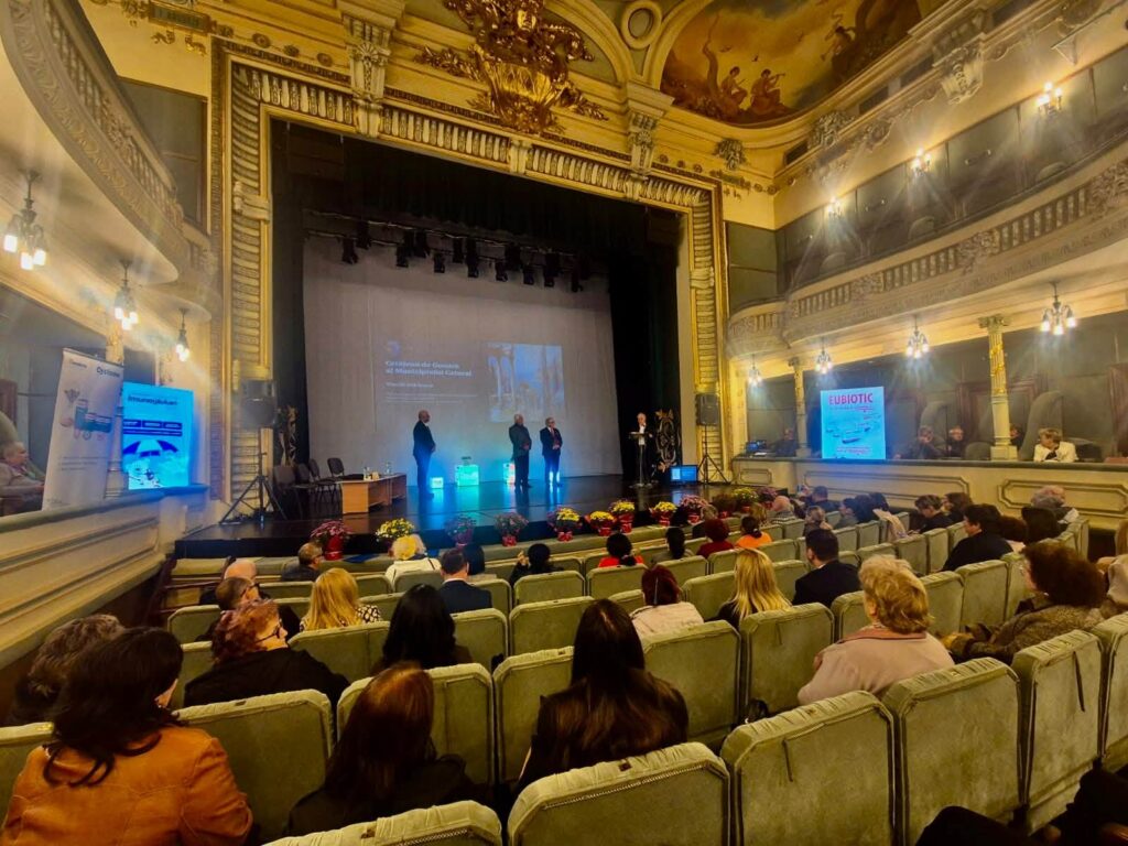 zilele medicale caracalene 855448873_1435557575426880_7456786494304022904_n - Jurnalul Olteniei – Știri din Craiova și Oltenia Panel discussion on a gilded, ornate theater stage with four speakers and a projection screen, audience in front